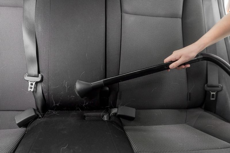 The process of cleaning the interior of a car from animal hair. A human hand is vacuuming the interior of the car.