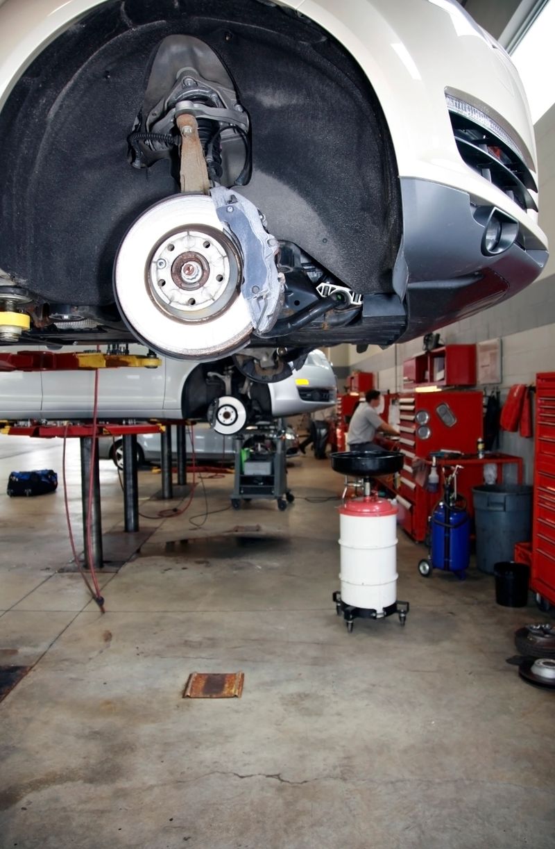 The interior of a car dealership repair facility, shows two cars on hoists.