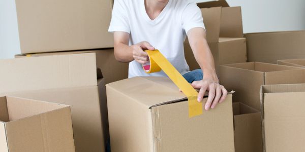 Man packing cardboard boxes with yellow tape indoors.