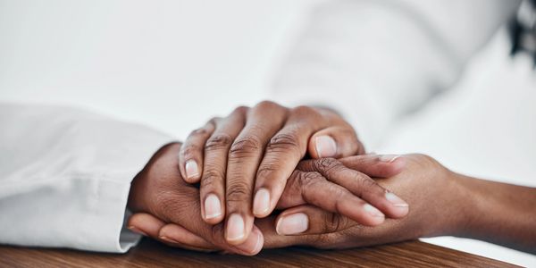 Two hands gently holding each other on a wooden surface.