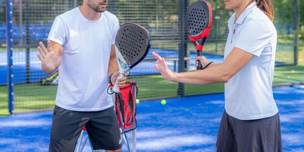 Two people playing padel on a blue court, preparing to hit the ball.