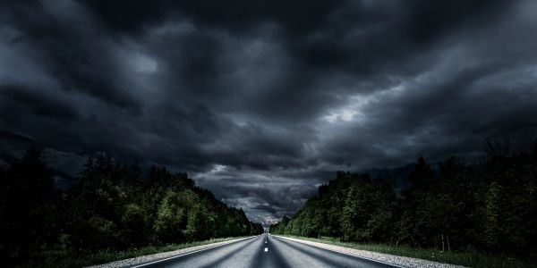 A dark, empty road stretches into the distance under a stormy sky.