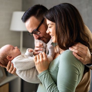 Parents lovingly hold and smile at their newborn baby indoors.