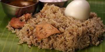 Traditional chicken biryani served on a banana leaf with boiled egg and side dishes.