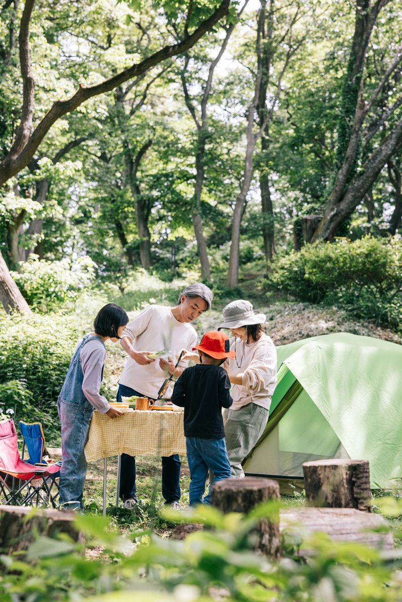 Wide shot of  Japanese family preparing to cook together in the great outdoors. With a well-organized camping table, they are set for a flavorful adventure.