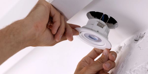 Hands installing a recessed ceiling light fixture.