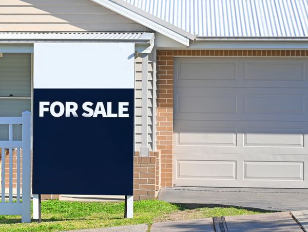 A 'For Sale' sign in front of a suburban house with a garage.