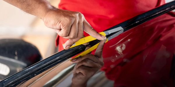 Person using a utility knife to cut a material on a glossy surface.