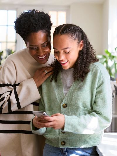 Two women happily looking at a phone in a bright kitchen.