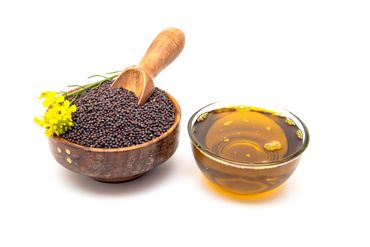Mustard seeds in a wooden bowl and mustard oil in a glass bowl.
