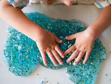 Child playing with blue glittery slime on white surface.
