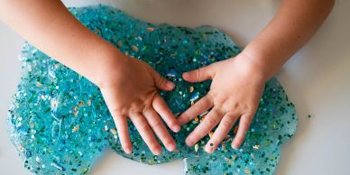 Child playing with blue glittery slime on white surface.