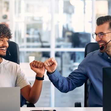 Two coworkers sharing a happy fist bump in an office.