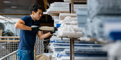 Worker handling stacked materials in a warehouse.