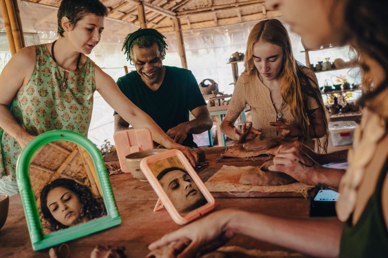 A diverse group of friends of many nationalities and ages participate in a pottery workshop and learning how to create face mask using clay.