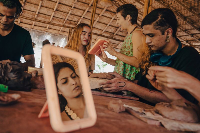 A diverse group of friends of many nationalities and ages participate in a pottery workshop and learning how to create face mask using clay.