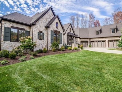 A stunning stone-clad home with elegant landscaping, lush green grass, and a spacious three-car