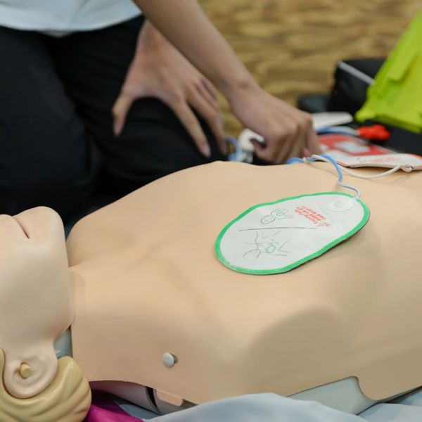 Person practicing CPR with a training mannequin and AED pads.