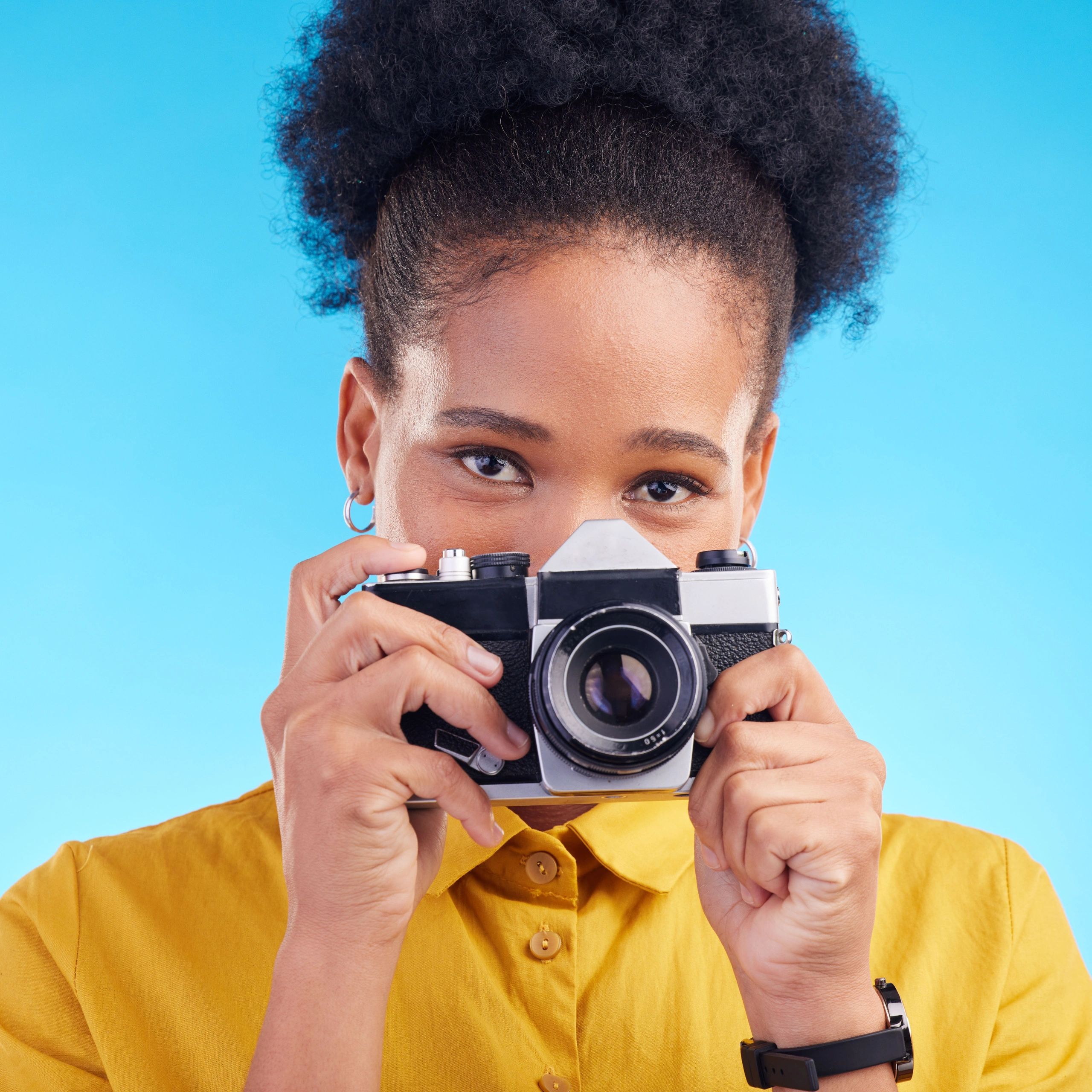 Person holding a vintage camera against a blue background.