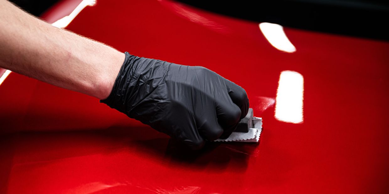 Hand in black glove polishing a shiny red car surface.