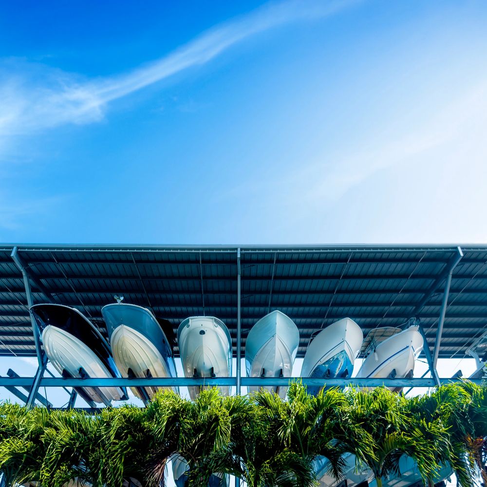 Boats stored upside down on a metal rack with palm trees below under a clear blue sky.