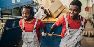 Two workers in red shirts and grey overalls in a recycling facility.