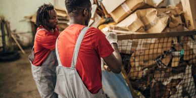 Two workers sorting recyclable cardboard in a warehouse.