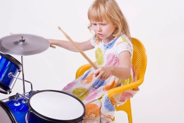 Young girl enthusiastically playing a drum set.