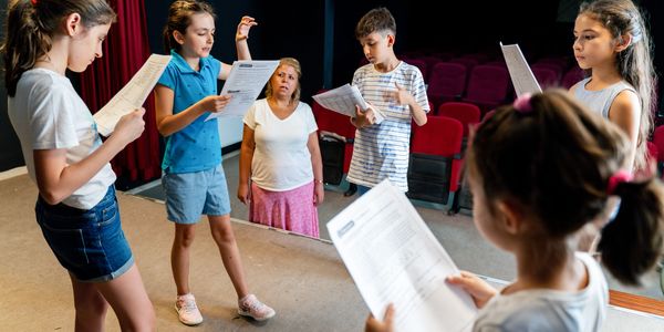 Group of kids rehearsing with a teacher on stage.