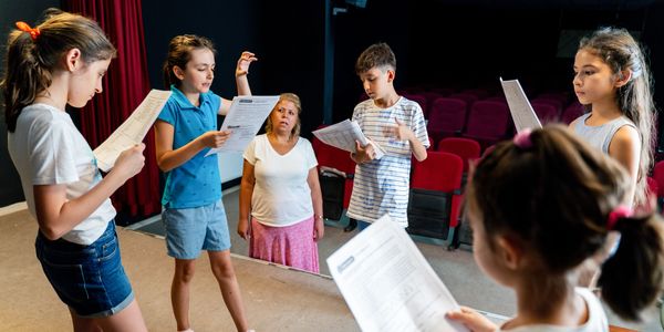 Children rehearsing a play with a teacher in a theater.