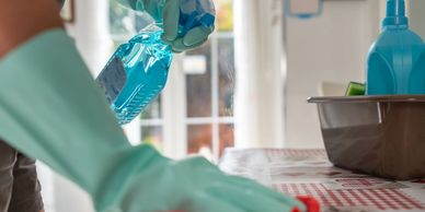 Person cleaning a table with spray and cloth wearing green gloves.