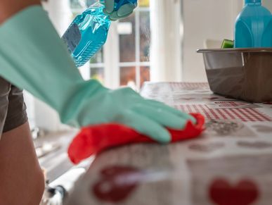 Person cleaning a table with spray and cloth wearing green gloves.