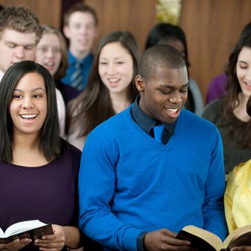 A diverse group of young adults singing and reading from books together.