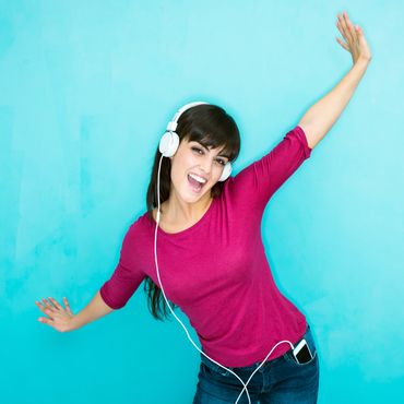 Young woman joyfully dancing with headphones on against a blue background.