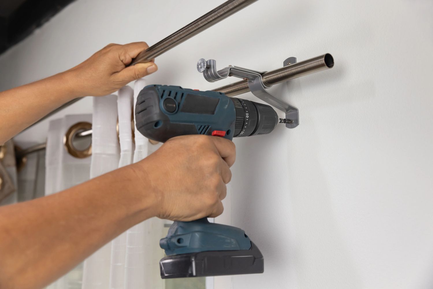 Person installing a curtain rod using a cordless drill.