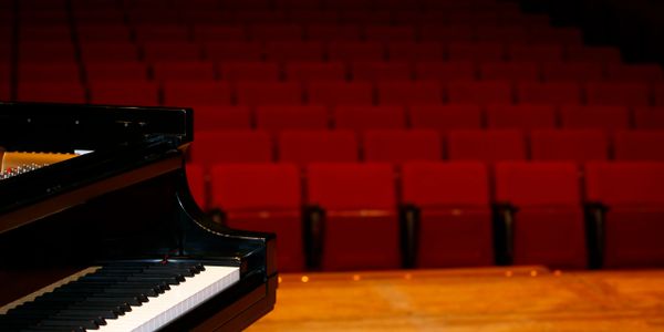 A grand piano on stage with empty red theater seats in the background.
