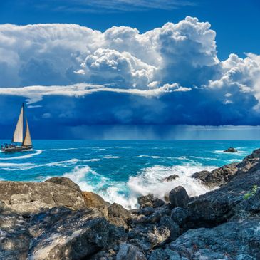 Sailboat on turquoise sea with dramatic storm clouds.