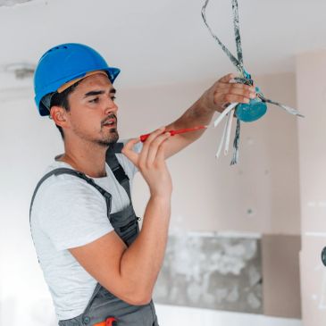 Smiling handyman with tools and a drill, wearing a yellow hard hat.