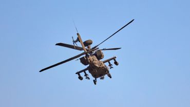 Military attack helicopter flying against a clear blue sky.
