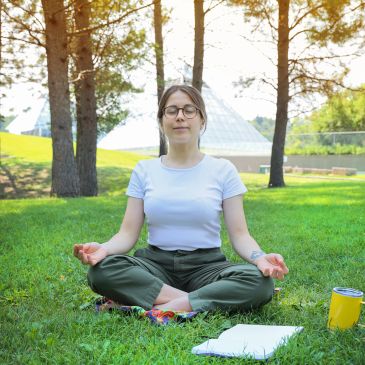 Woman meditating outdoors on grass in a serene park.