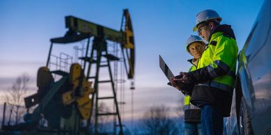Two engineers in safety gear inspecting an oil pumpjack at dusk.