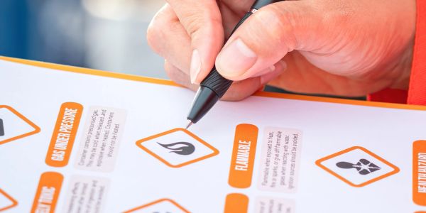 Hand holding a pen over a flammable hazard symbol on a checklist.