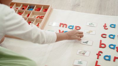 Child arranging colorful letters and picture cards on a mat for learning.