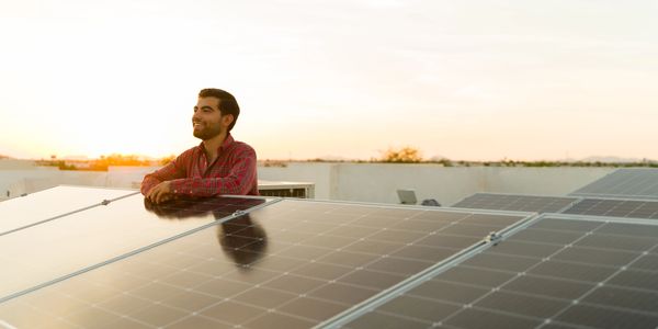 A man who is smiling while leaning on high end solar panels on his roof.