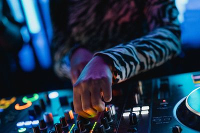 A DJ adjusting controls on a mixer with colorful lights.