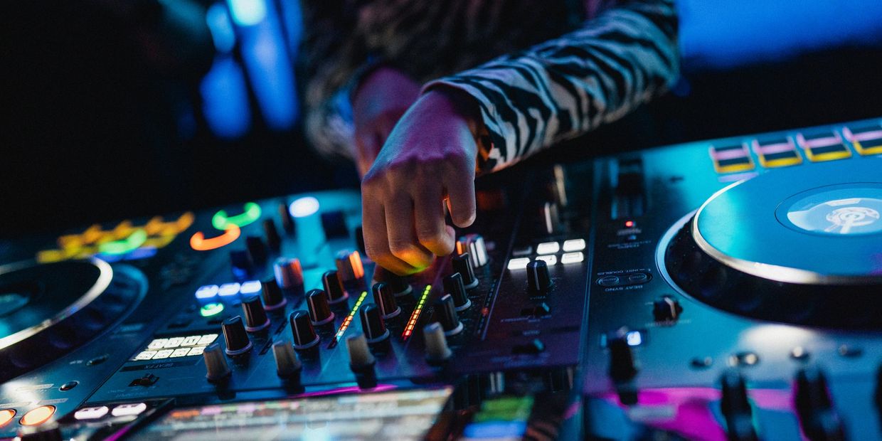 A DJ adjusts controls on a colorful mixer in a dimly lit club.