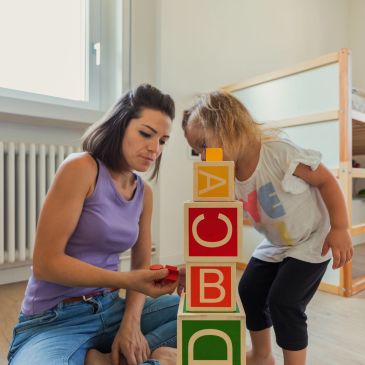 Mother and child playing with alphabet blocks indoors.