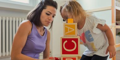 Woman and child playing with alphabet blocks indoors.