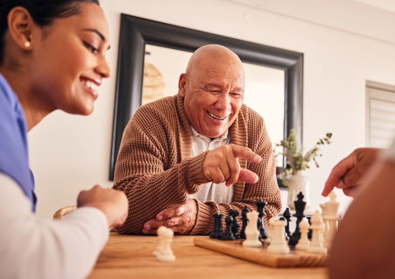 Senior man, nursing home and chess for game, competition and happy with friends, strategy and relax together. Elderly person, nurse and board for contest with mindset, excited smile or point at table