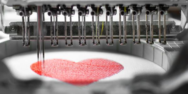 Machine embroidery stitching a red heart on fabric.